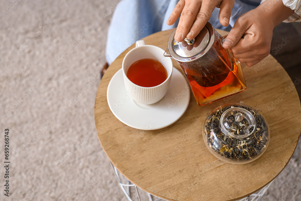 Young woman pouring hot tea into cup at home, closeup