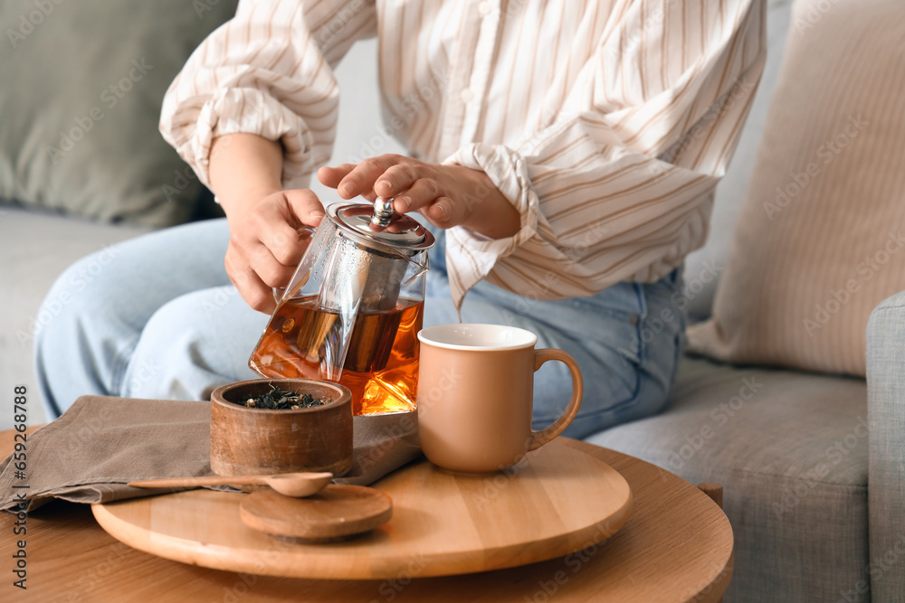 Young woman pouring hot tea into cup at home, closeup