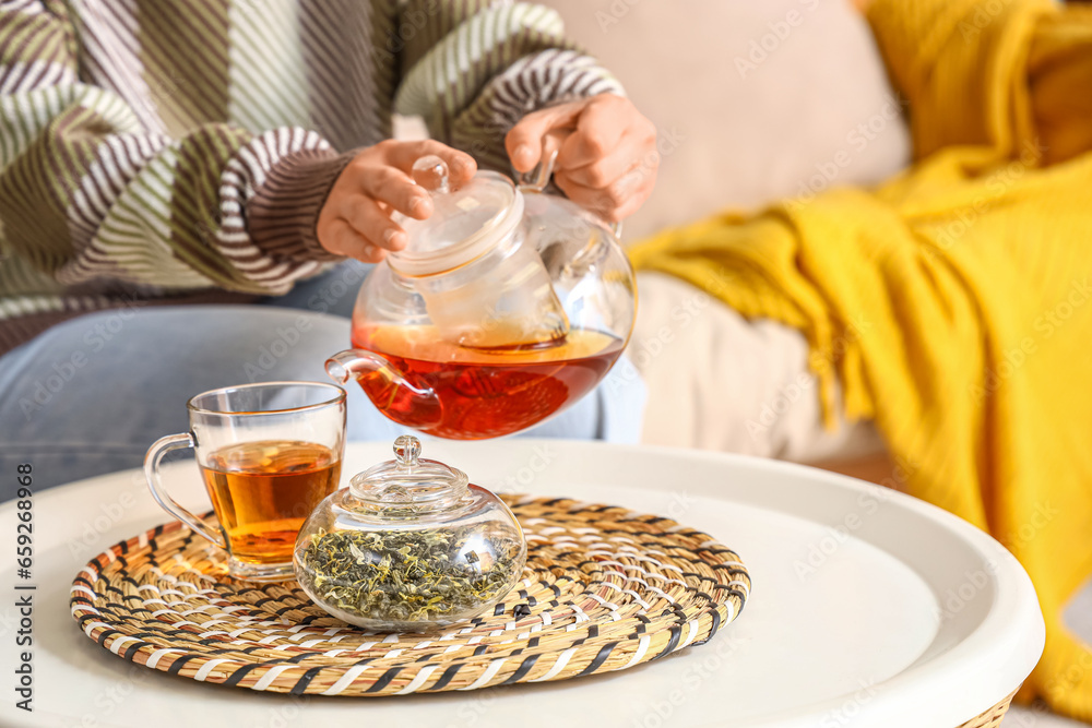 Young woman pouring hot tea into glass cup at home, closeup