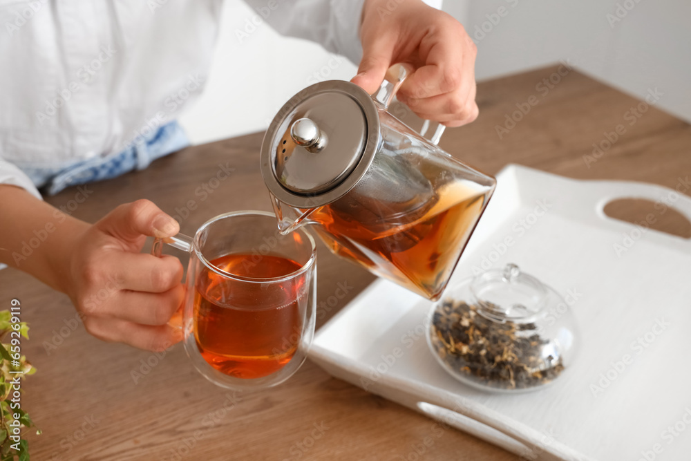 Young woman pouring hot tea into glass cup in kitchen, closeup