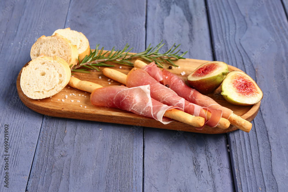 Board of tasty Italian Grissini with prosciutto, bread and figs on blue wooden background