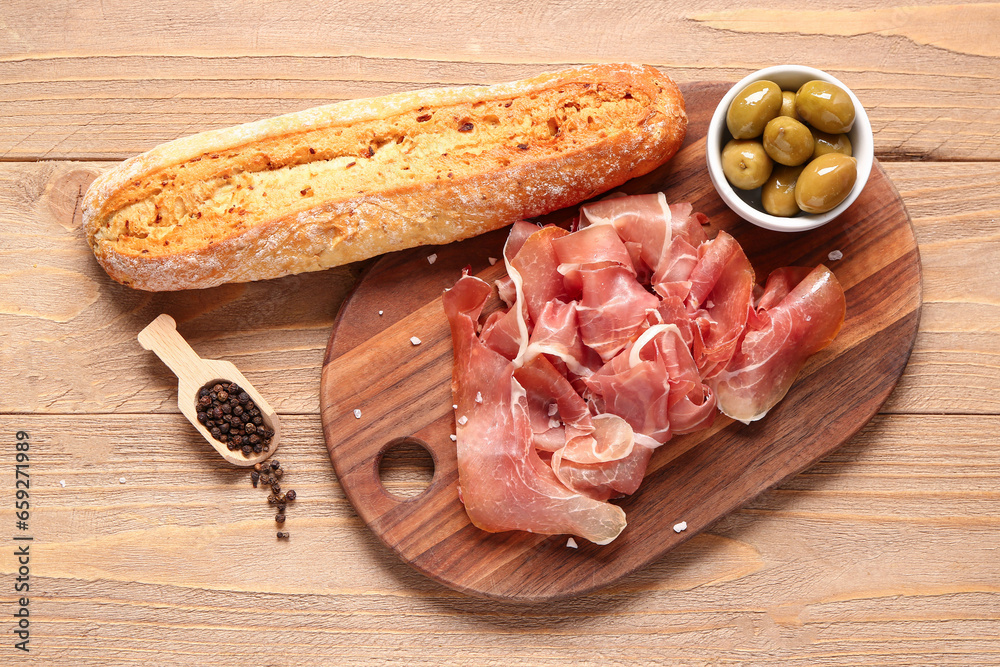 Board with slices of tasty prosciutto, olives and bread on wooden background