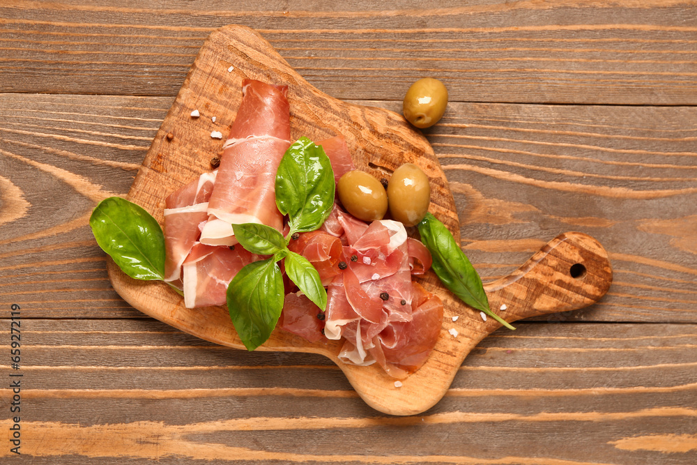 Board with slices of tasty prosciutto and olives on wooden background