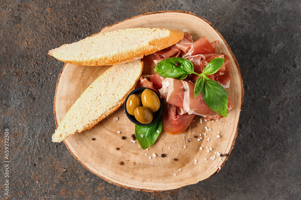 Wooden board with slices of tasty prosciutto and bread on brown background