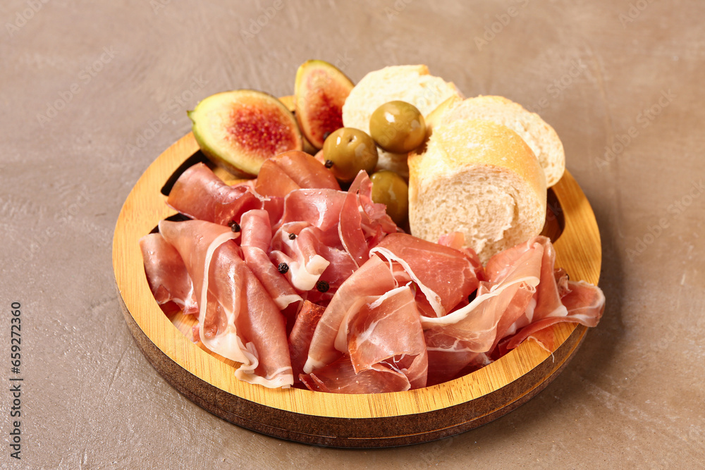 Wooden board with slices of tasty prosciutto and bread on brown background