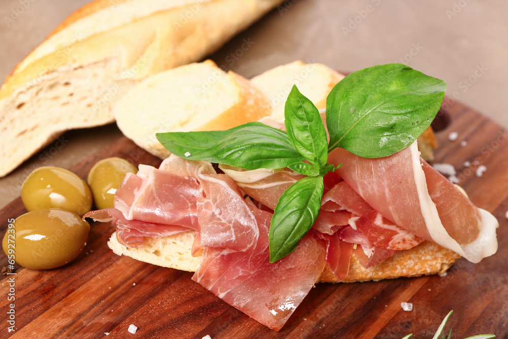 Wooden board of tasty sandwich with prosciutto on brown background