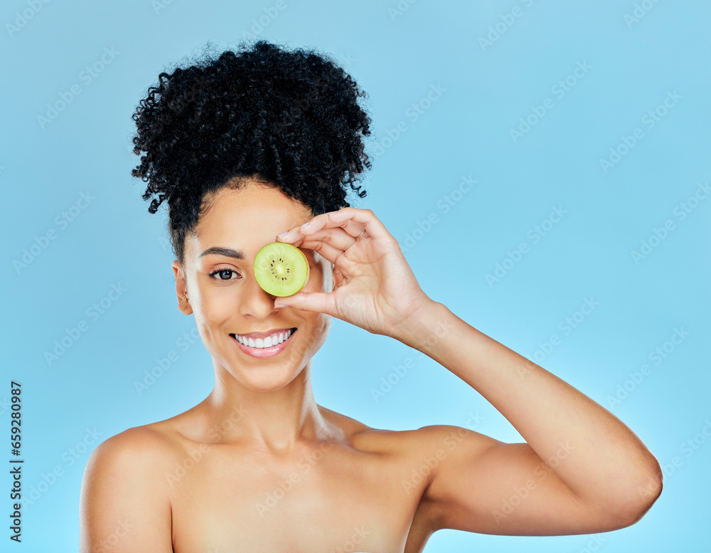 Portrait, skincare and happy woman with kiwi in studio for wellness, detox or natural cosmetics on blue background. Face, smile and female model with fruit for beauty, nutrition or dermatology care