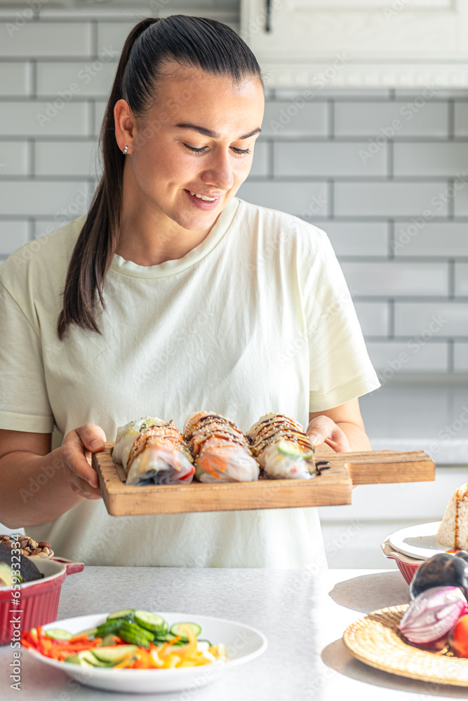 A young woman with spring rolls in rice paper in the kitchen.