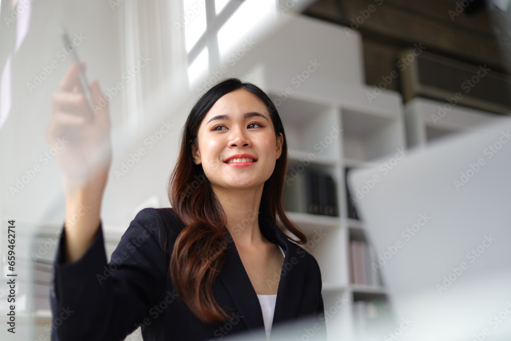 Asian businesswoman scheduling work strategy, planning work in the office with paper stickers on the glass.