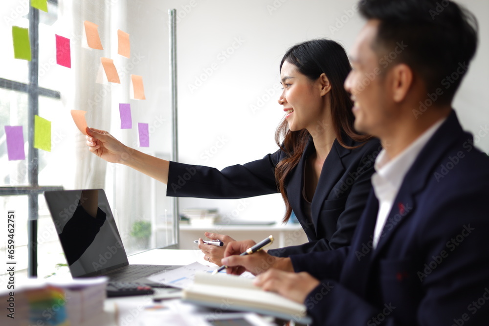 Businessmen and colleagues brainstorming scheduling business strategy, planning work in the office with paper stickers on the glass.