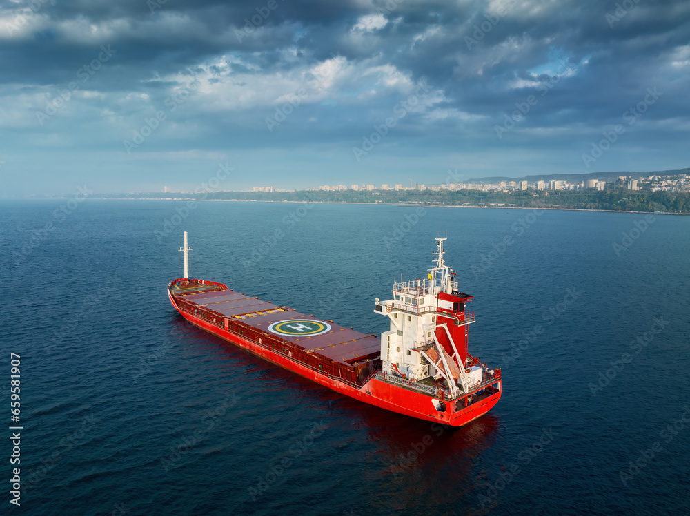 Sea sunrise over ocean horizon and sailing industrial cargo ship in deep blue open waters, aerial view