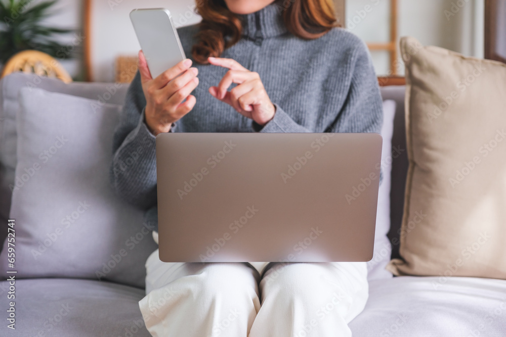 Closeup image of a young woman chatting on mobile phone while using laptop computer at home