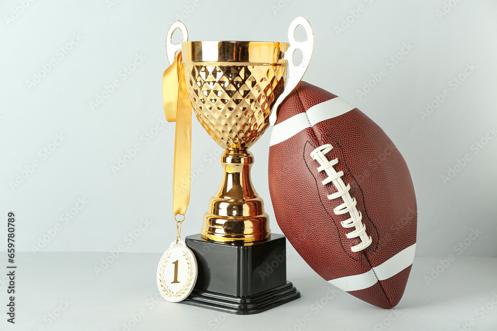 Gold cup with first place medal and rugby ball on light background