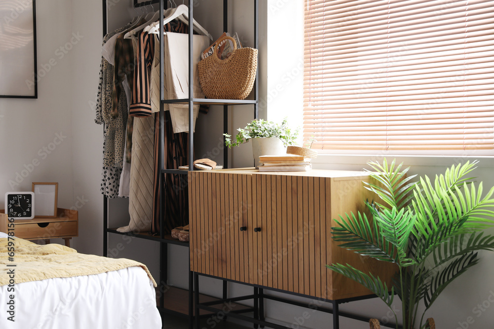 Interior of light bedroom with shelving unit and clothes