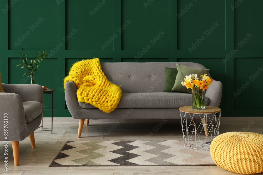 Interior of living room with grey sofa, armchair and narcissus flowers on coffee table