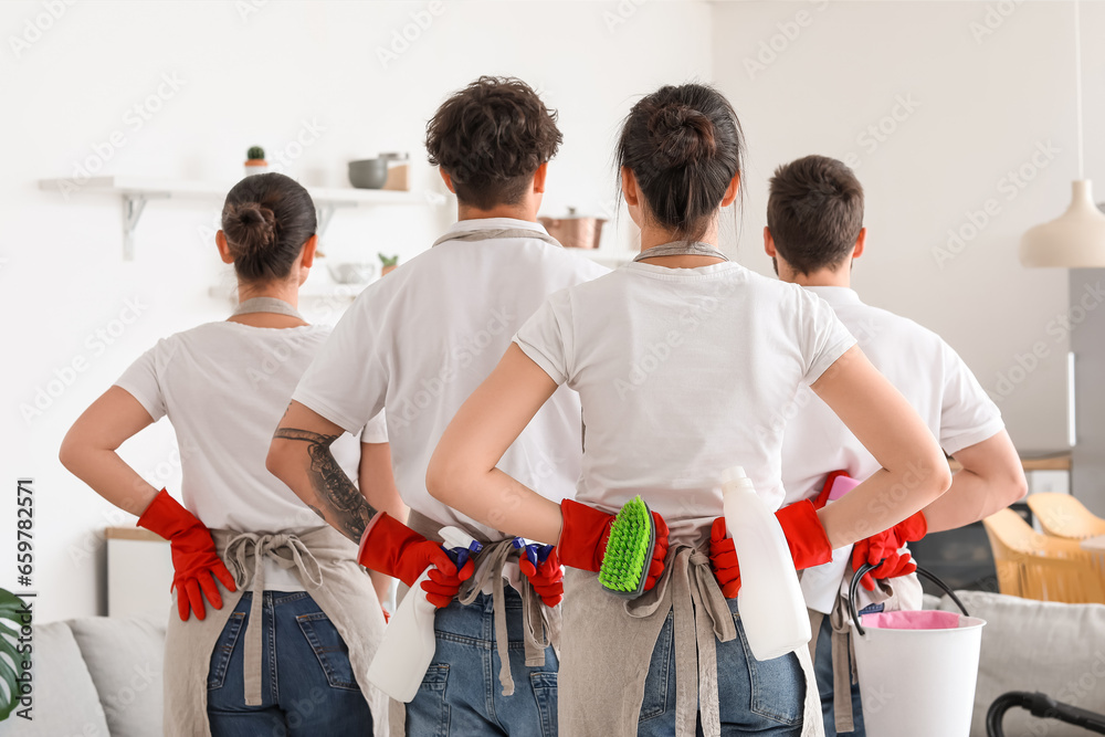 Young janitors with cleaning supplies in kitchen, back view