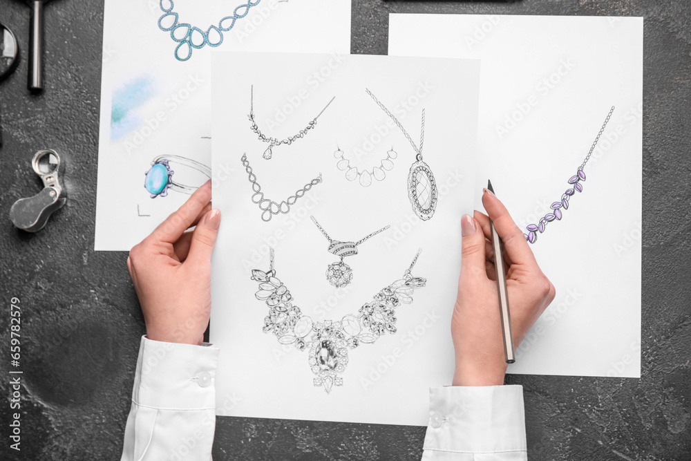 Female jeweler with drawings of adornment on dark table, top view