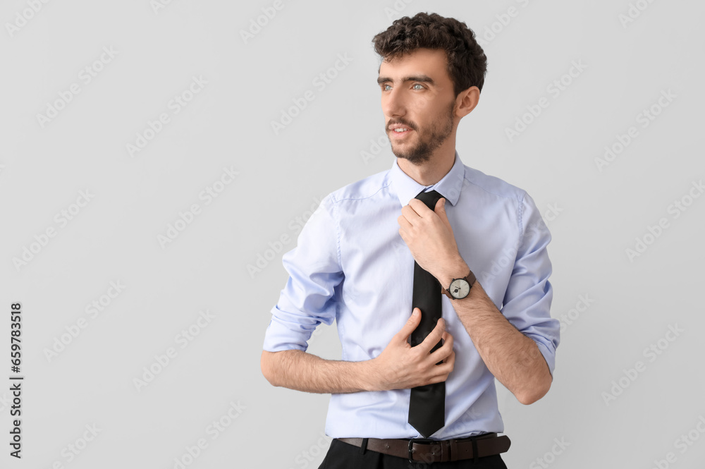 Young businessman fixing necktie on light background