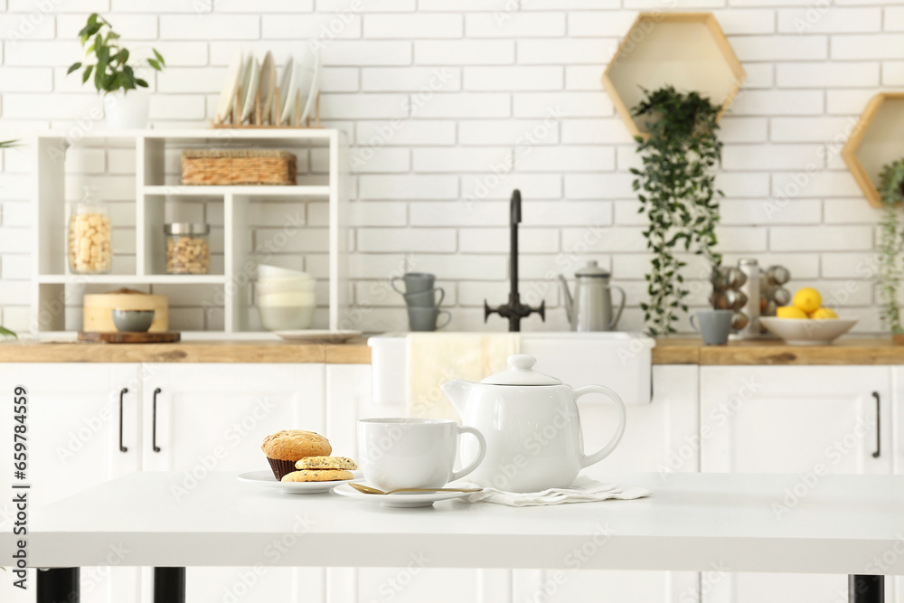 Interior of light kitchen with teapot, cup and snacks on table