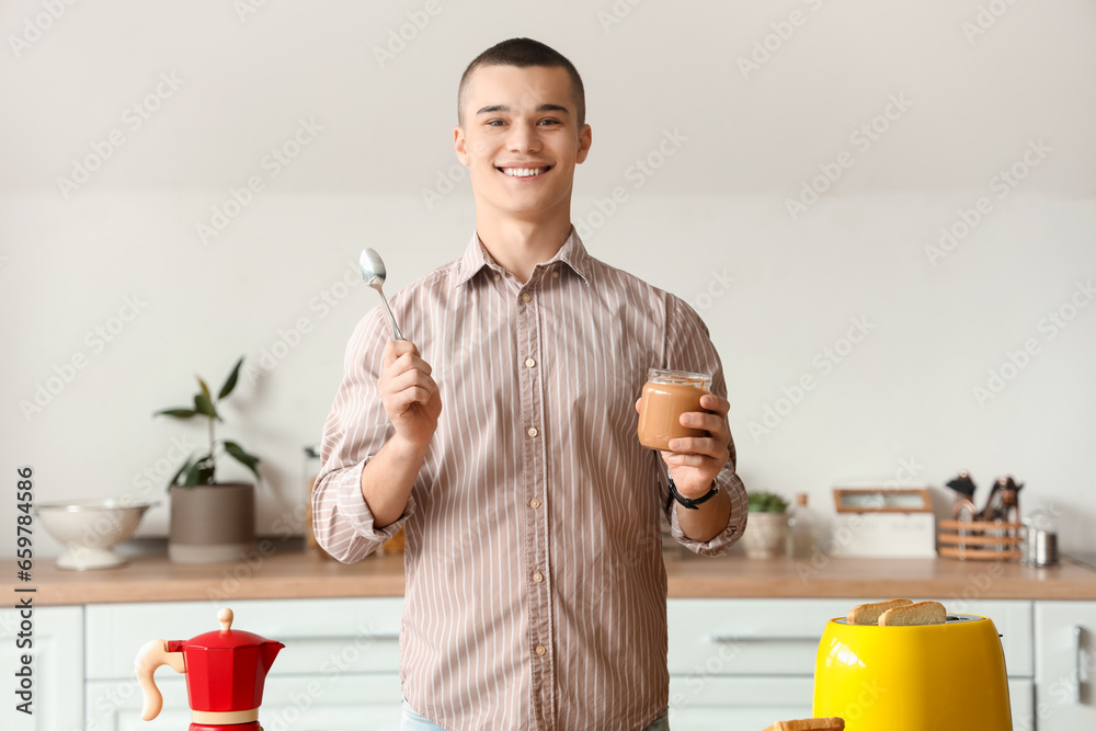 Happy young man with tasty nut butter in kitchen