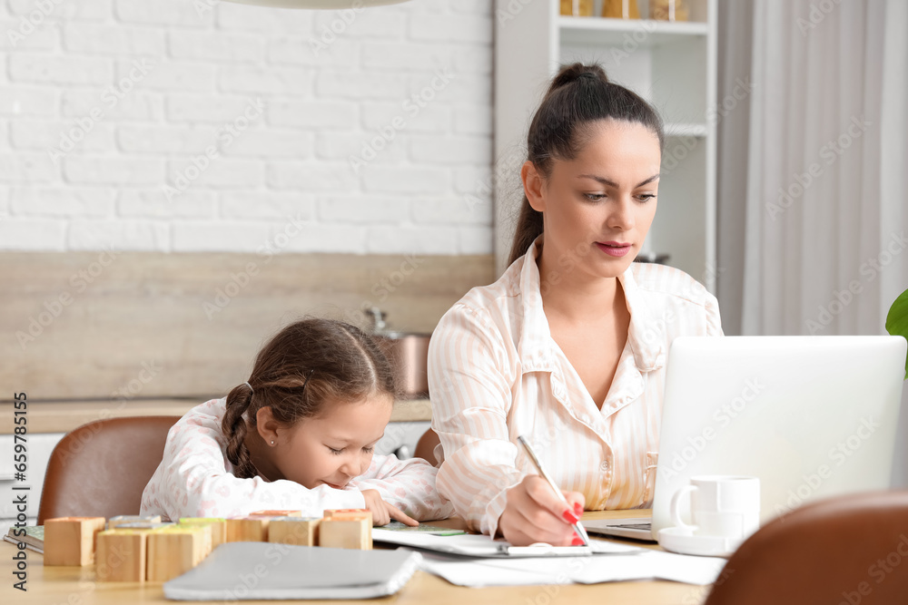 Working mother with her little daughter reading book in kitchen