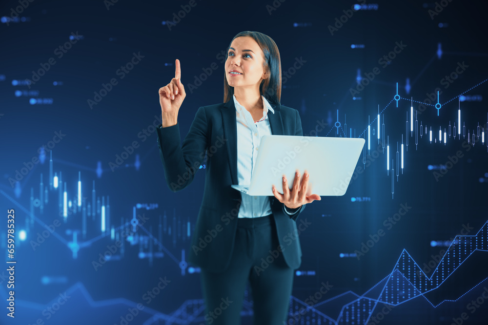 Attractive young european businesswoman with laptop pointing up at glowing candlestick forex chart and index hologram on blurry blue background. Trade and stats concept.