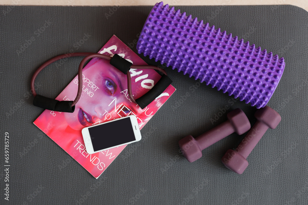 Sports equipment with mobile phone and magazine on fitness mat in gym, top view