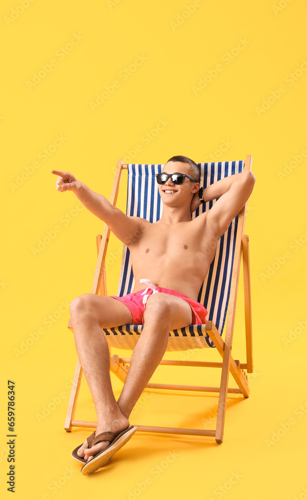 Teenage boy pointing at something in deck chair on yellow background