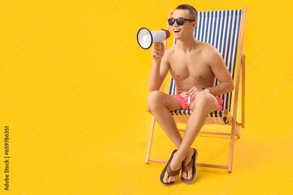 Teenage boy with megaphone in deck chair on yellow background