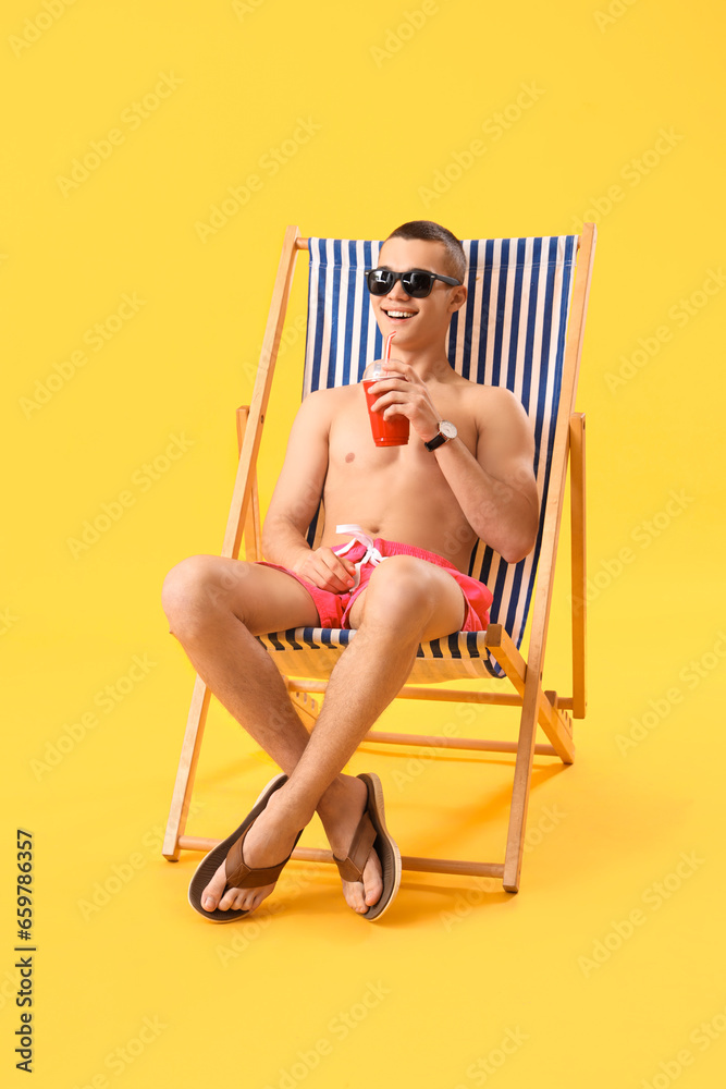 Teenage boy drinking soda in deck chair on yellow background