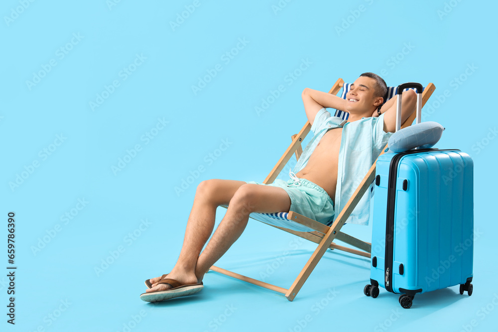 Teenage boy in deck chair and suitcase on blue background