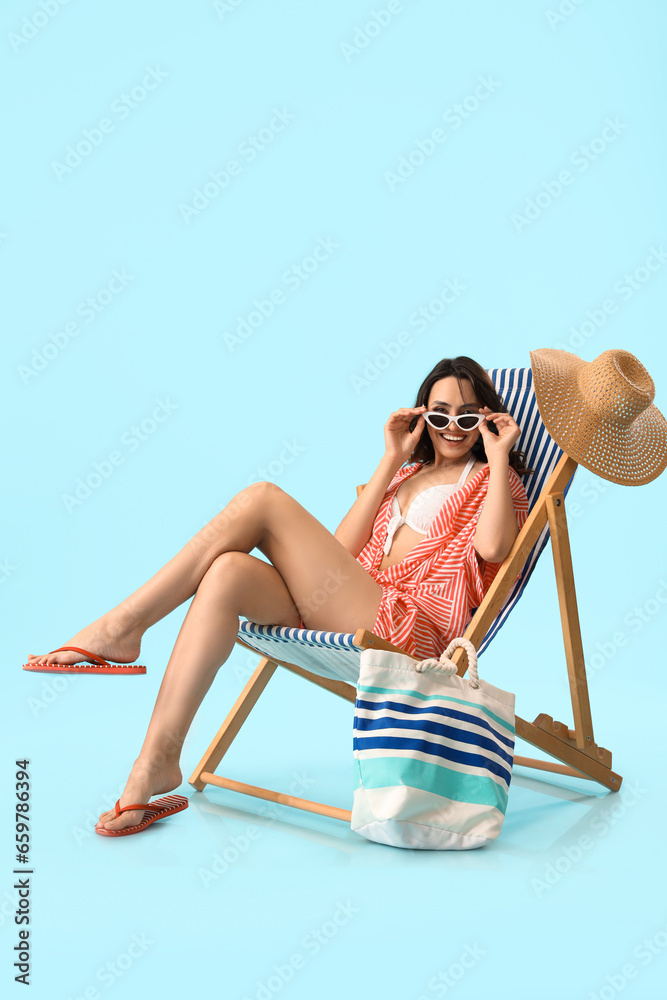 Young woman in deck chair on blue background