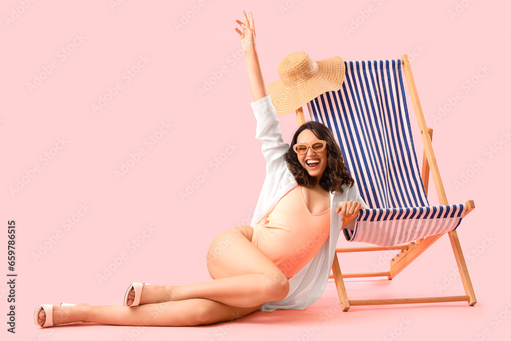 Young woman with deck chair sitting on pink background