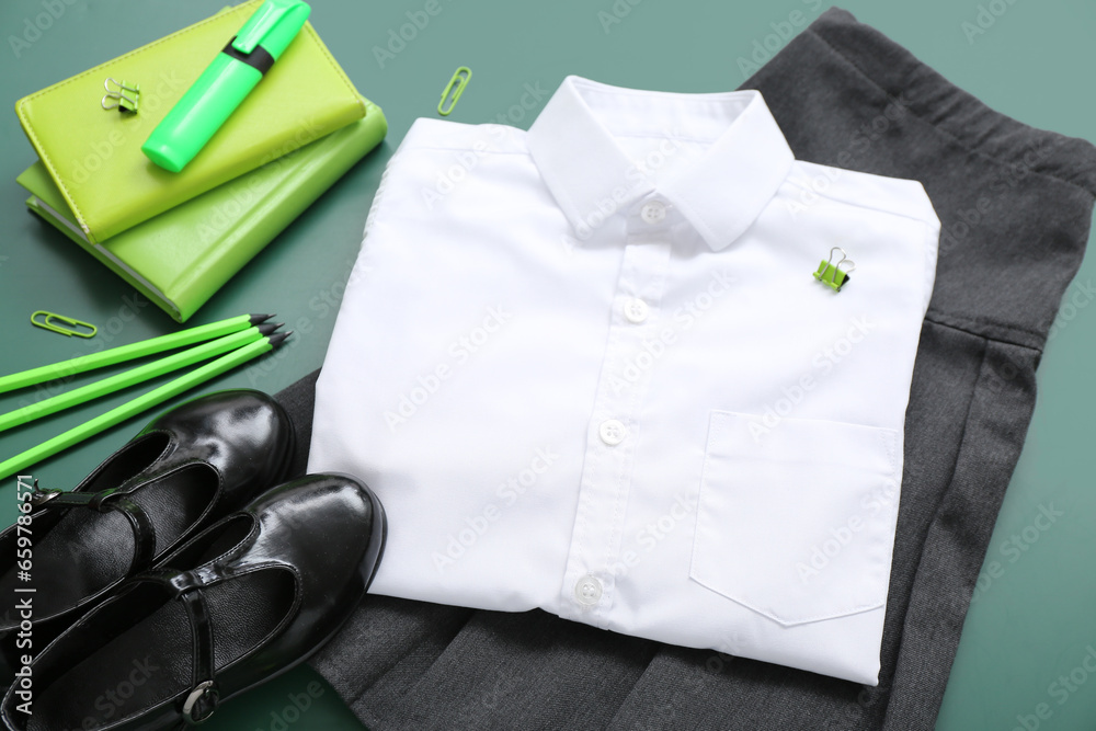 Different stationery and stylish school uniform on green chalkboard