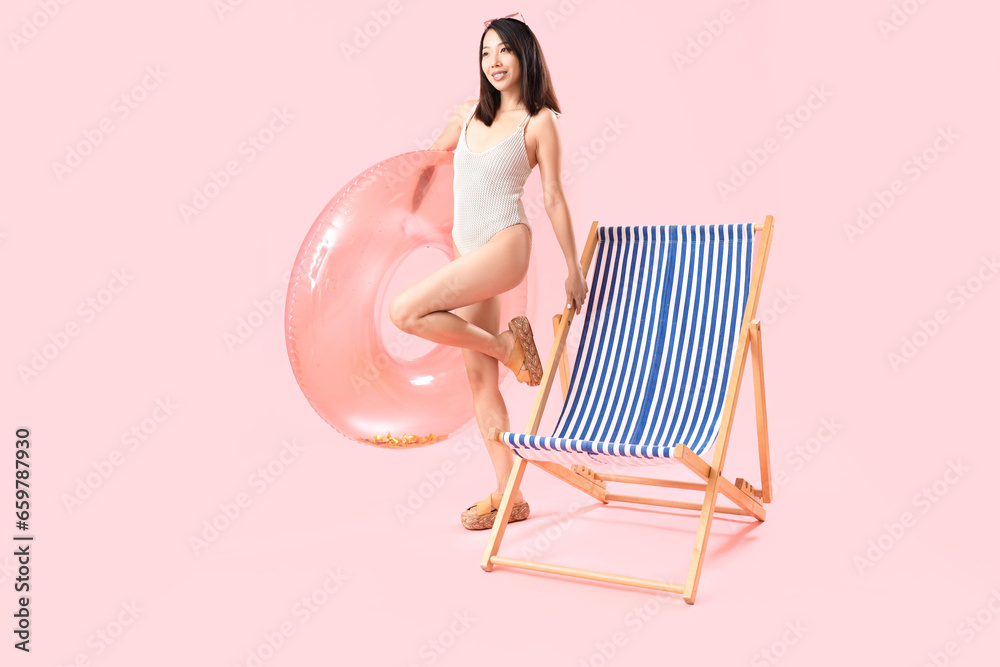 Beautiful Asian woman with swim ring and deck chair on pink background