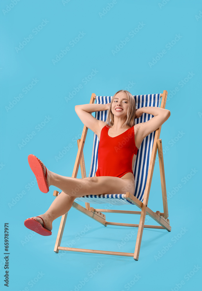 Beautiful young woman relaxing in deck chair on blue background