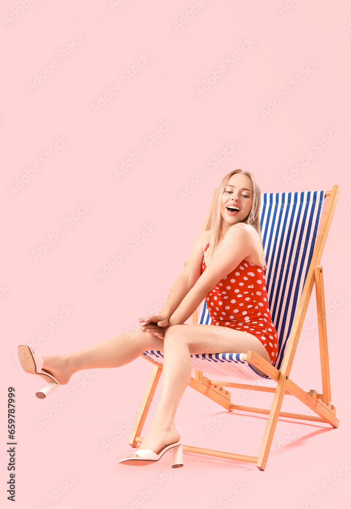 Beautiful young woman relaxing in deck chair on pink background