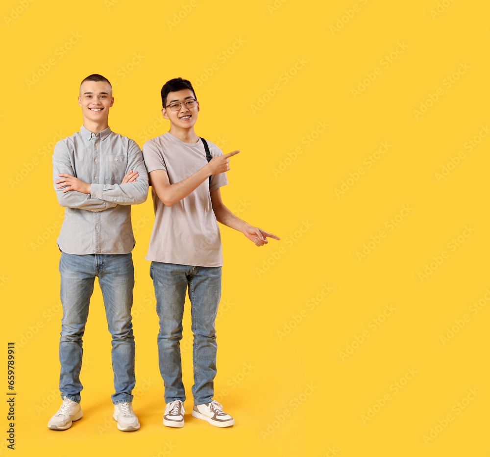 Happy male students with backpack pointing at something on yellow background