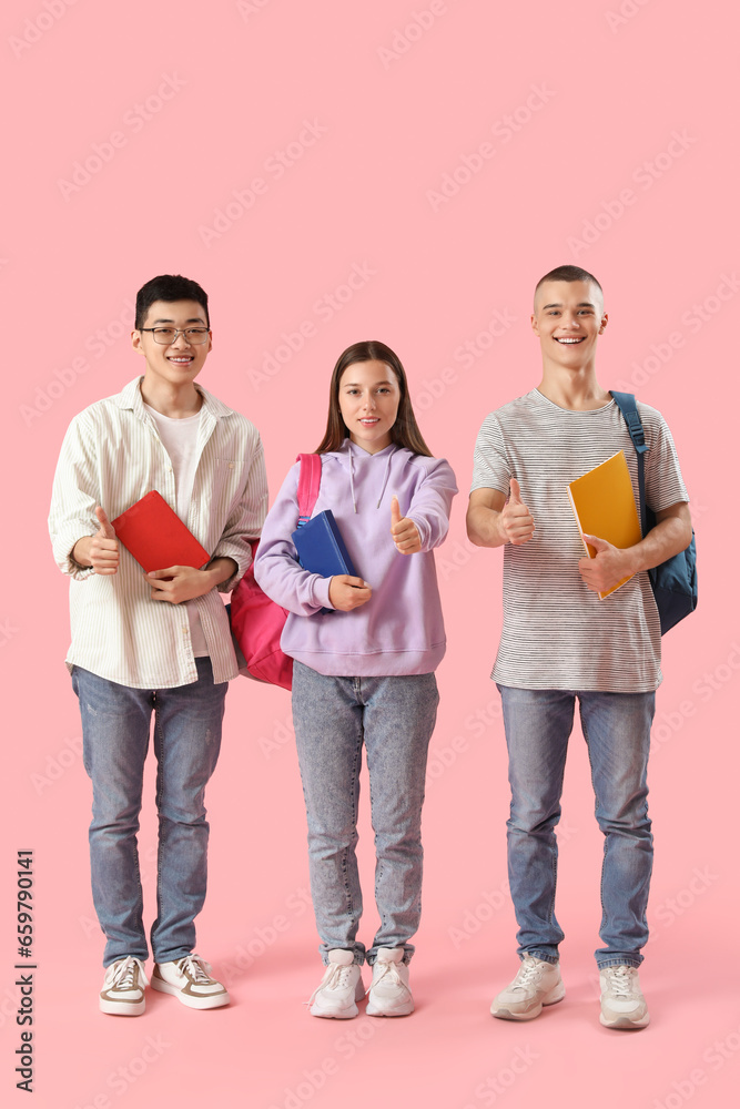 Happy students with backpacks and notebooks showing thumbs-up gesture on pink background