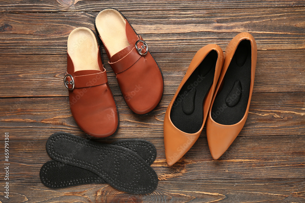 Stylish shoes with pair of orthopedic insoles on wooden background