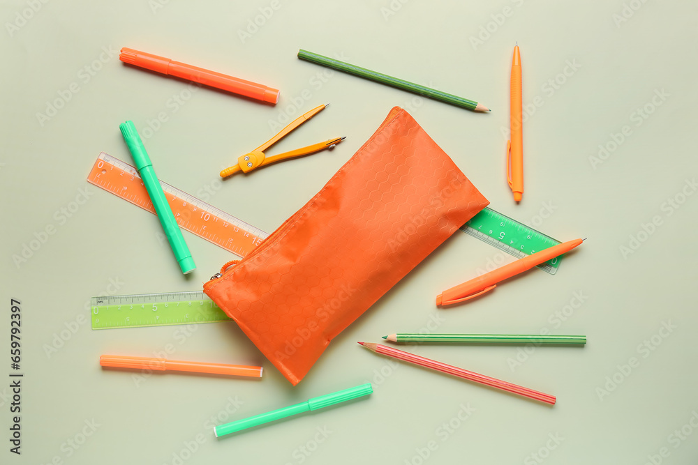 Orange pencil case with school stationery on green background