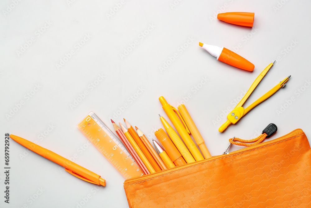 Orange pencil case with school stationery on grey background