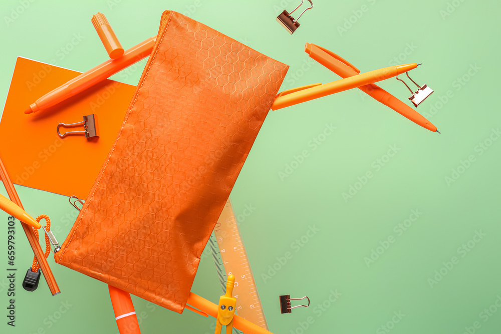 Flying orange pencil case and school stationery on green background