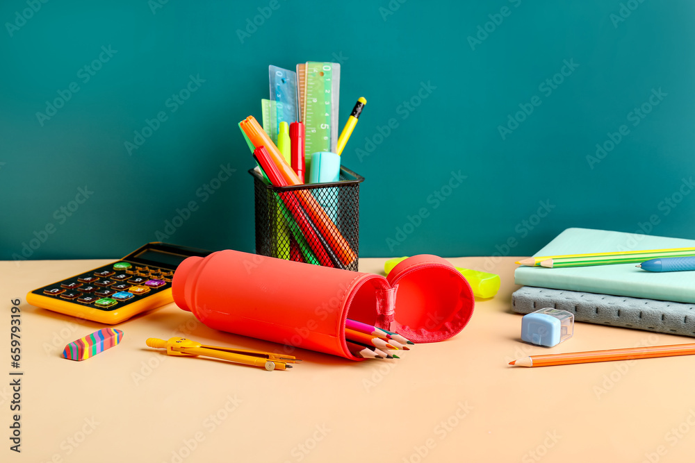 Red pencil case with school stationery on school desk near blackboard