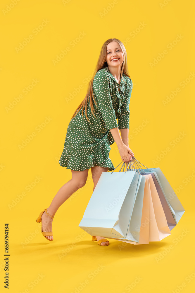 Pretty young woman with heavy shopping bags on orange background