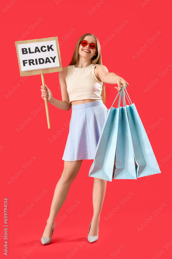 Pretty young woman holding shopping bags and sign with text BLACK FRIDAY on red background