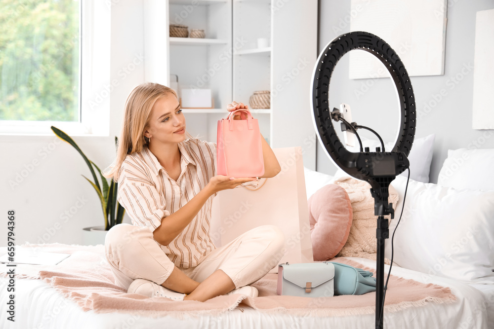 Beautiful young fashion blogger recording video while unpacking new bags at home