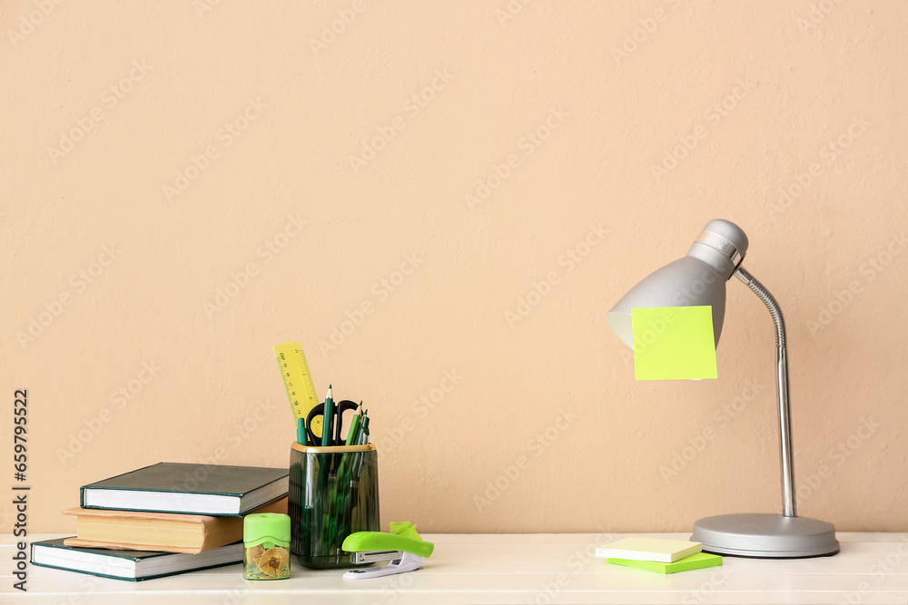 Holder with different stationery, books and lamp on light wooden desk