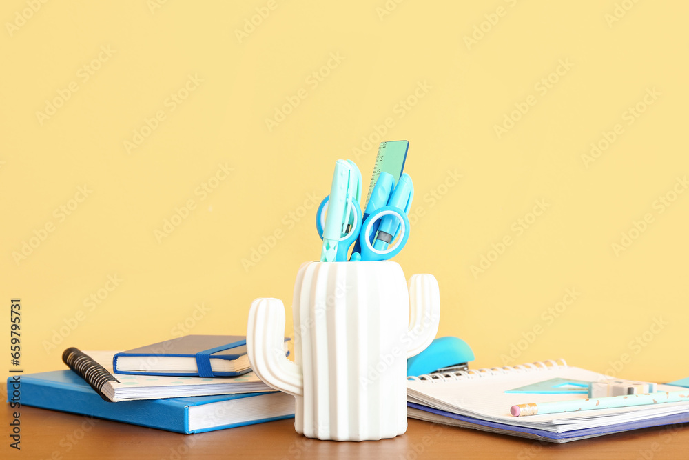 Holder with different stationery and notebooks on wooden desk