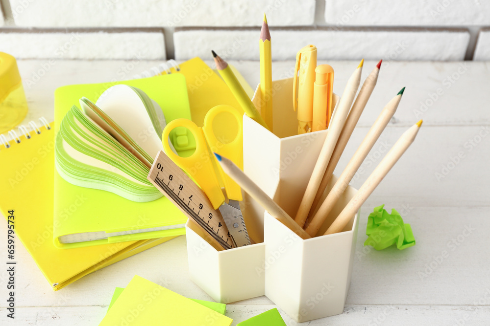 Holder with different stationery and notebooks on light wooden desk, closeup